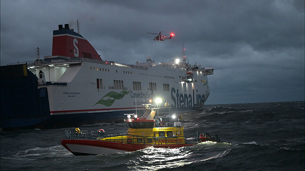 Fartyg till havs med helikopter ovanför samt räddningsbåt i förgrunden.