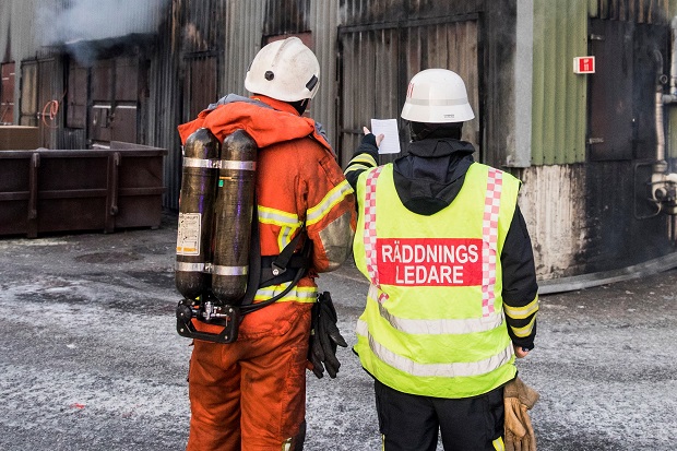 En brandman står tillsammans med en räddningsledare med ryggen mot kameran.
