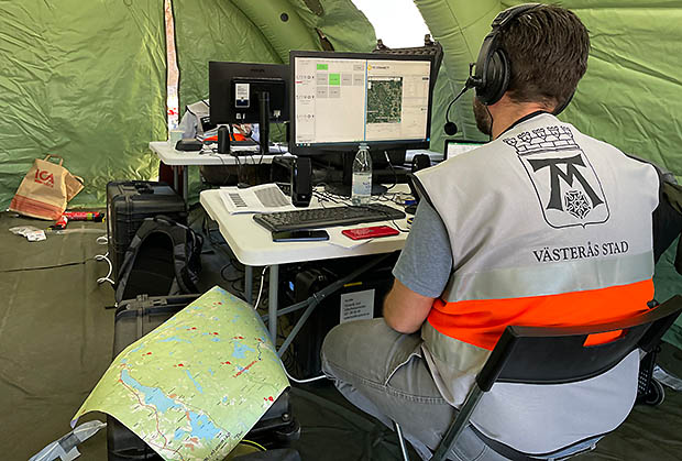 En sambandsoperatör med headset arbetar vid en dator i en tillfällig sambandscentral i ett tält.